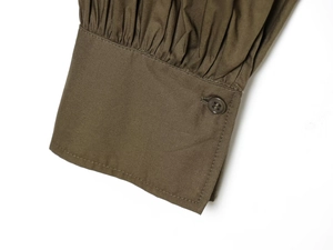 Detail of puffed sleeve cuff with pleats and a single button on a dark olive poplin shirt