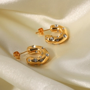 Detailed shot of gold hammered C-shaped earrings with clear zircons on beige silk