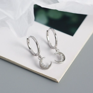 Close-up of silver crescent moon earrings with sparkling zircons and circular studs