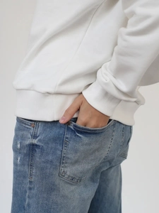 Dettaglio dell'orlo a coste e del polsino della felpa bianca con jeans blu casual