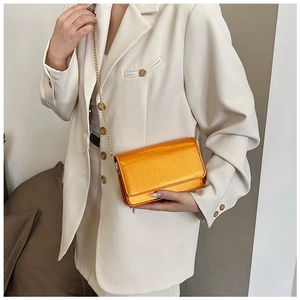Detail of bright orange crossbody bag with gold chain strap on a white blazer outfit