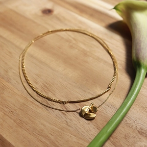 Double-layered gold-plated brass necklace with irregular pendant on a wooden background