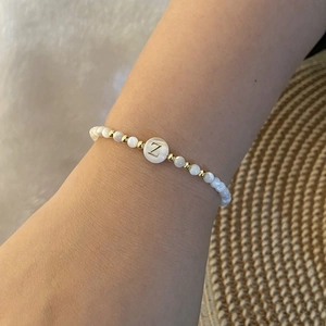 Detailed shot of white beaded shell bracelet with golden letter Z charm on wrist