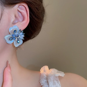 Close-up of elegant blue and white flower stud earrings with crystals on female model