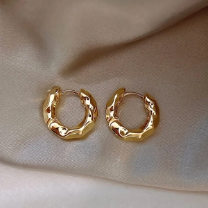Orecchini a cerchio dorati con trama martellata irregolare su elegante seta beige