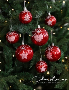 Close-up of red Christmas baubles with white painted heart and star patterns on a tree