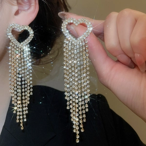 Detailed view of silver needle heart earrings with sparkling rhinestone tassels worn by a model
