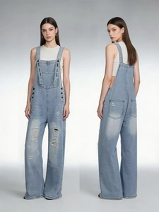 Detail of light blue distressed denim overalls featuring wide-leg cut and ripped knees