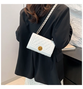 Detail of white quilted crossbody bag featuring gold chain strap and metal turn-lock