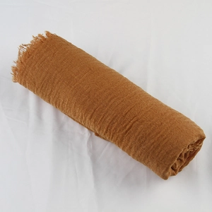 Macro detail of caramel crinkled cotton linen scarf showing soft fringe and fabric texture