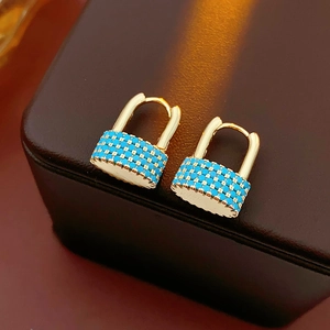 Close-up of gold-plated lock-shaped earrings set with blue turquoise stones on leather