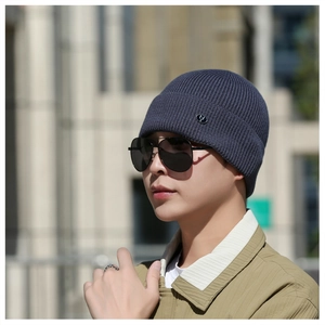 Close-up of a navy blue ribbed knit beanie with a metallic logo badge on a male model