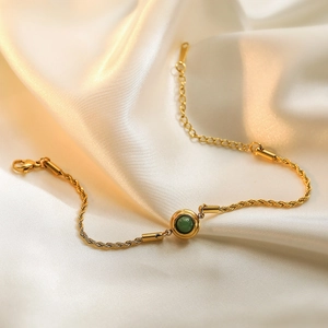 Gold plated twisted chain bracelet with a round green gemstone on white silk