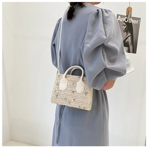 Side view of straw handbag featuring floral embroidery and white leather strap
