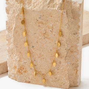 Détail du collier en titane doré avec petits pendentifs en losange posé sur une pierre