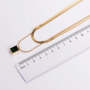 Macro shot of gold snake chain with green zircon pendant next to a metric ruler