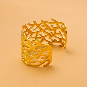 Macro view of wide gold-finished cuff bracelet featuring an intricate cutout branch texture