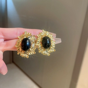 Close-up of gold metal floral earrings with black enamel worn on a finger to show detail