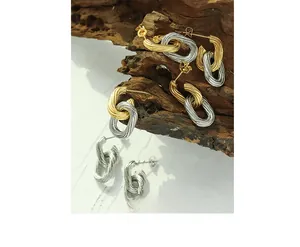 Macro detail of oval textured chain earrings in gold and silver finish on a wood block