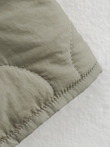 Detailed close-up of olive green quilted fabric and reinforced edge stitching on jacket