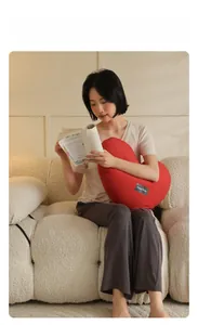 Cozy red heart-shaped cushion held by a model on a soft fleece sofa in a warm home setting