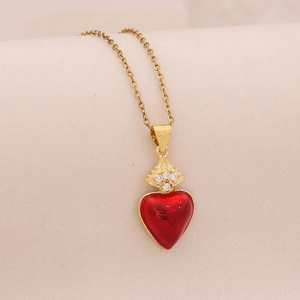 Macro shot of gold necklace featuring red heart pendant with crown and crystal detail