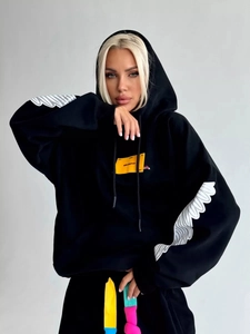 Oversized black hoodie with yellow embroidery and white sleeve patterns on a model
