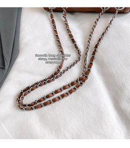 Detail of silver metal chain interwoven with brown leather strap on a quilted bag
