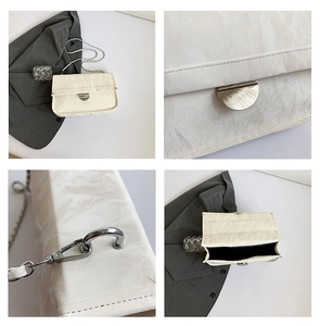 Detail of cream white pleated bag featuring silver metal twist lock and chain strap
