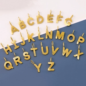 Set of 26 gold textured stainless steel alphabet pendants arranged on a dual-tone background