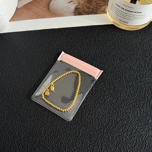 Golden beaded bracelet with two bells inside a pink-sealed anti-oxidation jewelry bag