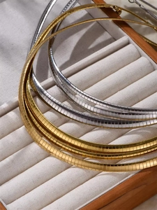 Macro view of gold and silver snake bone chain chokers on beige velvet jewelry tray