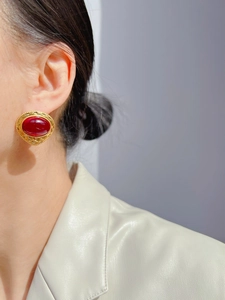 Detail view of large vintage-style gold relief earrings with oval red gemstone on model