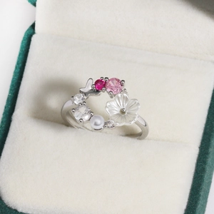 Detail of floral butterfly ring with white petals and pink zircons in a green gift box