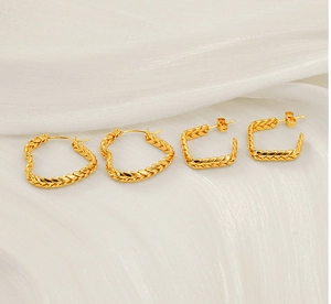 Detailed view of gold wheat ear woven heart earrings and square studs on white silk