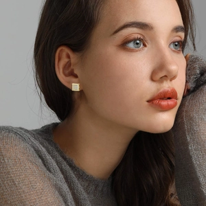 Square gold-plated stud earrings with pavé cubic zirconia worn by model on grey backdrop