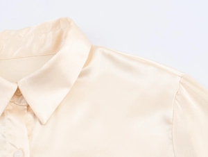 Nahaufnahme der beigen Satinbluse mit Kragendetails und glatter Seidentextur