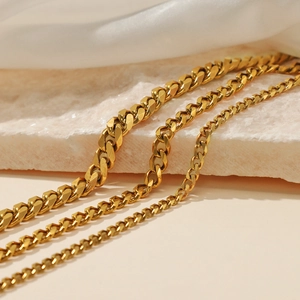 Three gold-plated Cuban link necklaces in varied sizes displayed on silk and stone