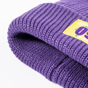 Purple ribbed knit beanie with yellow street-style patch showing thick wool texture