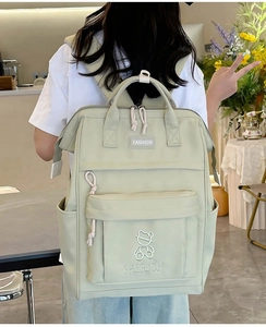 Close-up of light green school backpack with multiple pockets and bear embroidery details