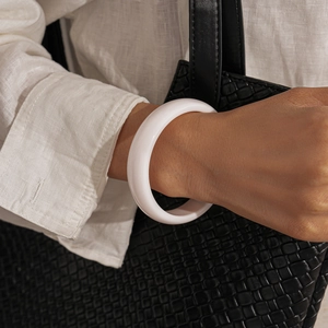 Detail of white resin bangle with polished finish worn on wrist with linen shirt