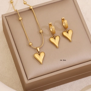 Polished gold heart pendant necklace and earrings set on a premium display stand