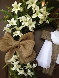 Close-up of Easter wreath with white lilies, burlap bow and wooden cross on vine base