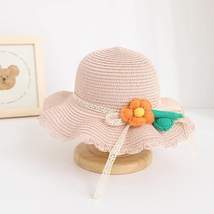Detail of pink straw sun hat for children with lace tie and orange flower decoration