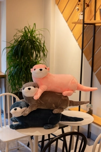 Soft plush otter toys in pink, brown, and blue colors stacked on a white round table