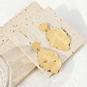 Detail of golden irregular fringe earrings displayed on beige travertine stone blocks
