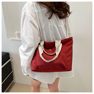 Detail of red nylon tote bag with wide geometric woven shoulder strap shown on model