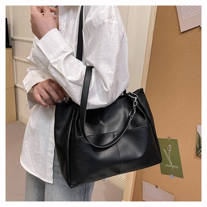 Dettaglio di una grande borsa tote in morbido PU nero con catena metallica su una modella