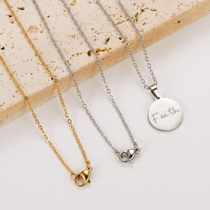 Detailed shot of gold and silver Faith engraved round pendant necklaces on a stone base