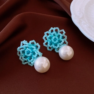 Detailed close-up of blue beaded flower earrings with large white pearls on brown silk